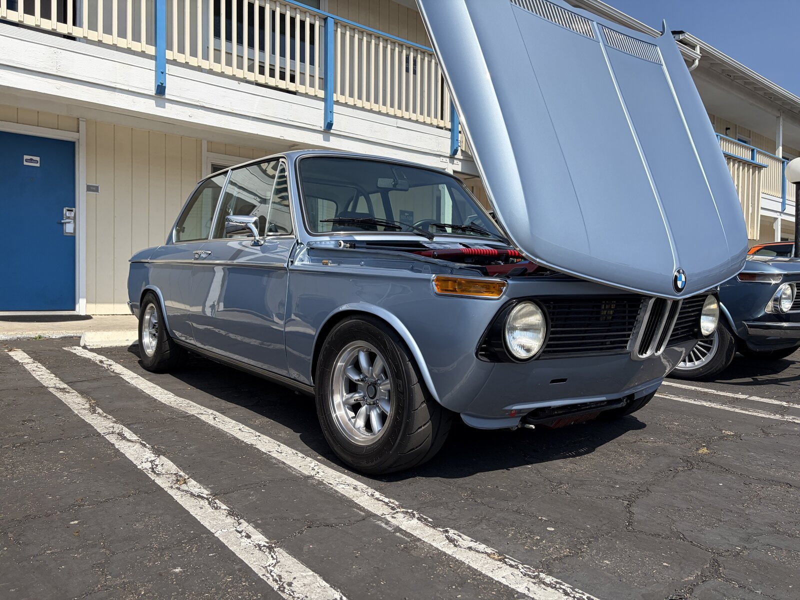 A light blue BMW 2002 with its hood raised at the car show
