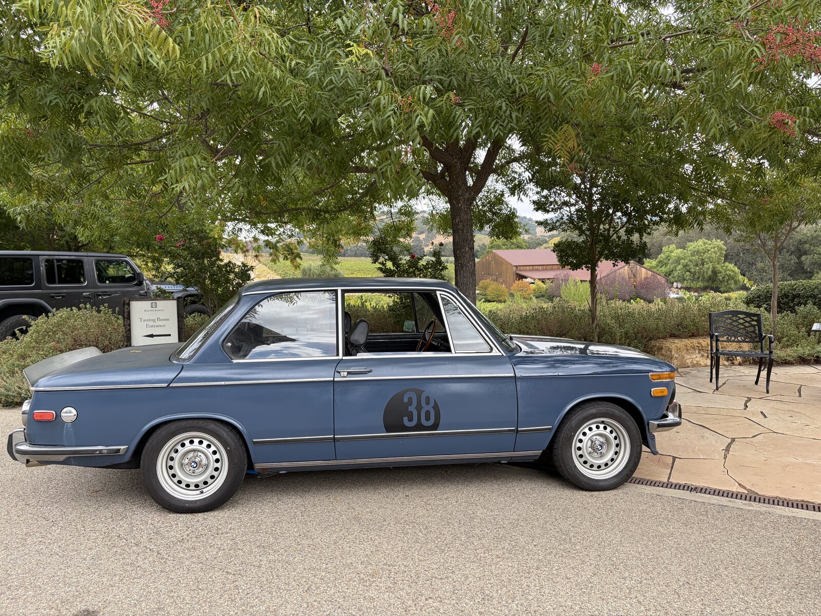Enthusiasts gathered around an open hood beneath the trees