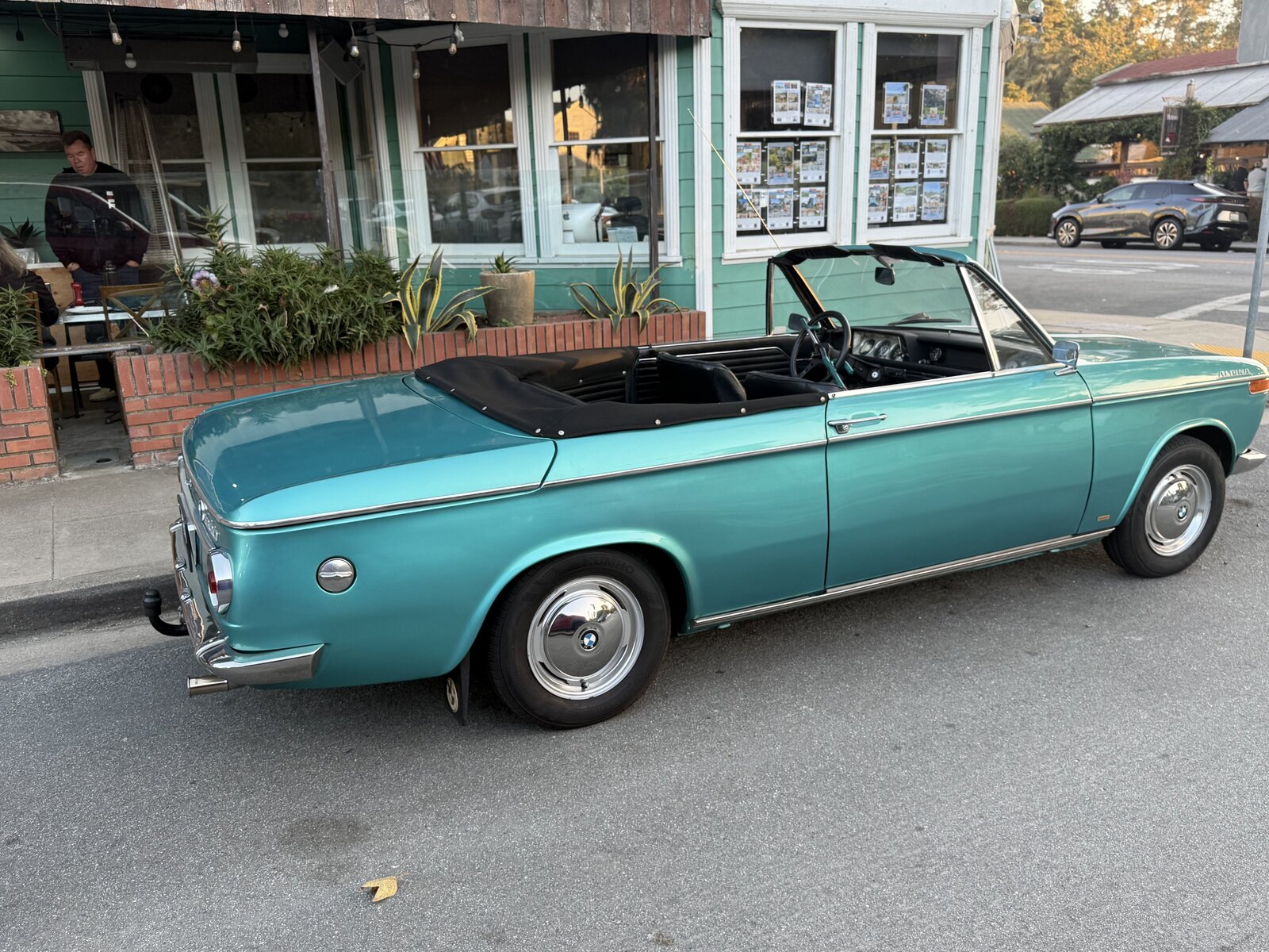 A turquoise BMW convertible parked beside a local storefront