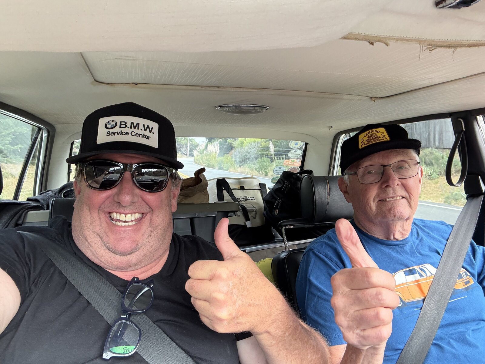 Two enthusiasts sharing smiles and a thumbs-up from inside their car